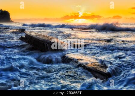 Farbenprächtiger orangefarbener Sonnenaufgang über dem Pazifik vor den Nordstränden von Sydney bei stürmischem Wetter. Stockfoto