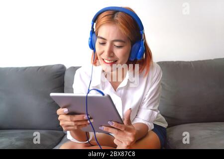 Asiatische junge Frau ist glücklich, zu Hause zu arbeiten. Sie nutzt ein Tablet, um mit ihren Kollegen in einem Unternehmen Video-Chats zu führen. Stockfoto