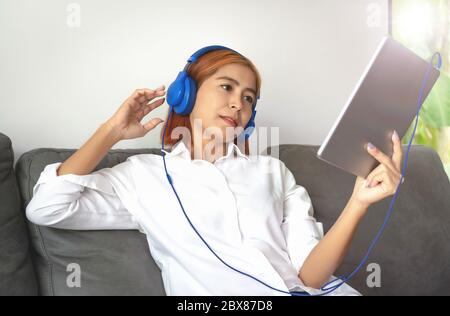 Asiatische junge Frau ist glücklich, zu Hause zu arbeiten. Sie nutzt ein Tablet, um mit ihren Kollegen in einem Unternehmen Video-Chats zu führen. Stockfoto