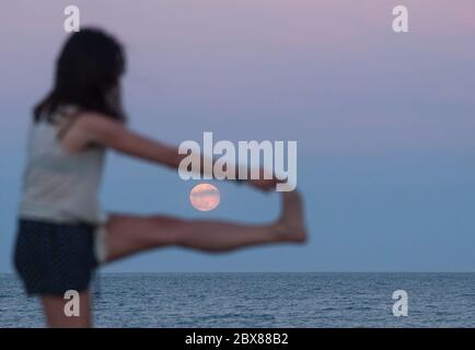 Malaga, Spanien. Juni 2020. Der Erdbeervollmond, als Teil einer Mondfinsternis, steigt über den Horizont, während eine Frau am Strand von Malagueta inmitten der Lockerung der Coronavirus-Krankheit (COVID-19) Beschränkungen übt. In diesem Monat Juni sind die Erdbeer-Vollmond- und Halbmondfinsternis am 5. Juni das erste astronomische Ereignis, das die Menschen sehen können. Während dieses Monats wird auch eine Sonnenringfinsternis am 21. Juni zu sehen. Quelle: SOPA Images Limited/Alamy Live News Stockfoto