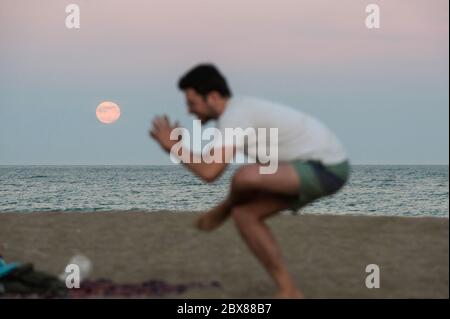 Malaga, Spanien. Juni 2020. Der Erdbeervollmond, als Teil einer Mondfinsternis, steigt über den Horizont, während ein Mann am Malagueta Strand inmitten der Lockerung der Coronavirus-Krankheit (COVID-19) Beschränkungen übt. In diesem Monat Juni sind die Erdbeer-Vollmond- und Halbmondfinsternis am 5. Juni das erste astronomische Ereignis, das die Menschen sehen können. Während dieses Monats wird auch eine Sonnenringfinsternis am 21. Juni zu sehen. Quelle: SOPA Images Limited/Alamy Live News Stockfoto