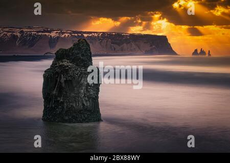 Dramatischer Himmel über Reynisfjara Strand, Island. Sonnenstrahlen, die durch die Wolken scheinen, weiße Wellen, die den schwarzen Sandstrand waschen. Stockfoto