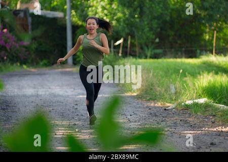 Outdoor-Lauftraining - junge glückliche und engagierte asiatische chinesische Frau joggt im schönen Stadtpark oder Landweg bei Sonnenuntergang genießen fitnes Stockfoto