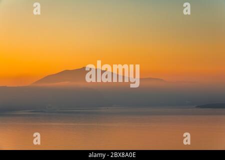 Die ruhige Oberfläche des Meeres nach Sonnenuntergang. Oranger Himmel und Nebel über dem bergigen Ufer Stockfoto