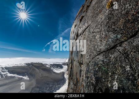 Vertikale Steinwand des Berges auf der rechten Seite werden nass im Frühling, wenn Wasser beginnt, von der Spitze nach unten zu laufen. Helle Sonne und noch viel Schnee Stockfoto