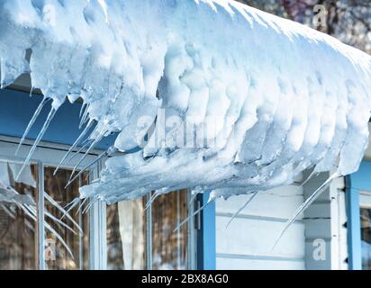 Nahaufnahme von Schnee und gebogenen Eiszapfen, die vom Dach der traditionellen schwedischen Holzhütte in Lappland, Nordschweden, hängen. Stockfoto