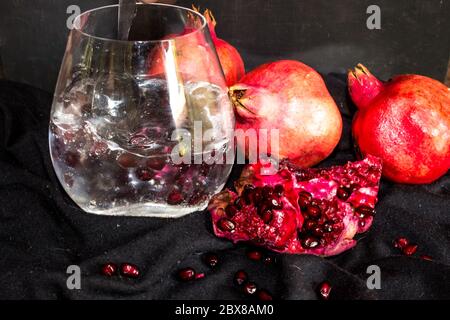 Ein Gin und Tonic, garniert mit einer großen Menge Granatapfelgruben, mit Granatäpfeln, auf schwarzem Hintergrund Stockfoto