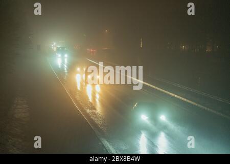 Viele schnelle Autos fahren in beide Richtungen auf der Autobahn in starkem dichten Nebel am späten dunklen Abend, warmer Herbst, Europäische Autobahn E4, außerhalb von Umea Stadt, Stockfoto