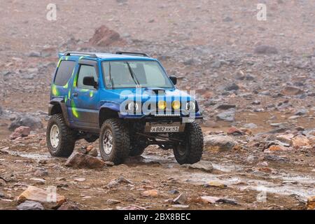 Japanischer SUV Suzuki Jimny Fahren auf felsigen Mount Road auf Hintergrund vulkanischen Landschaft. Aktivurlaub, Reiseziele, Offroad-Reise in regnerischen w Stockfoto