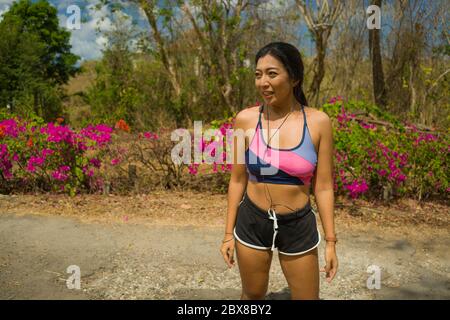 Junge schöne müde und atemlos Läufer asiatische Frau erschöpft und verschwitzt nach hartem Laufen Training im Trail Road Park in Fitness und gesunde Natu Stockfoto