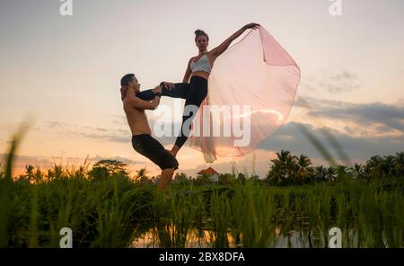 Im Freien Sonnenuntergang acroyoga Workout - junge glücklich und fit Paar üben acro Yoga-Übung auf schönen Reisfeld genießen Natur und gesunden Lebensstil Stockfoto