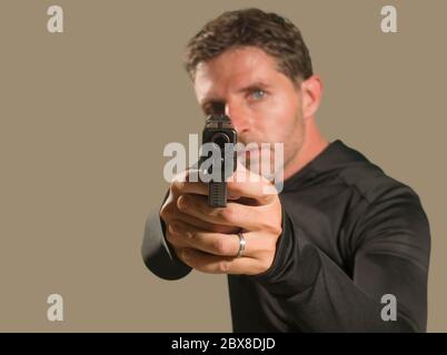 Flache Tiefe des Fokus Aktion Porträt von schweren und attraktiven Hitman oder Spezialagenten Mann hält Waffe zeigt die Handfeuerwaffe auf die Kamera isoliert o Stockfoto