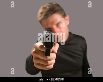 Flache Tiefe des Fokus Aktion Porträt von schweren und attraktiven Hitman oder Spezialagenten Mann hält Waffe zeigt die Handfeuerwaffe auf die Kamera isoliert o Stockfoto