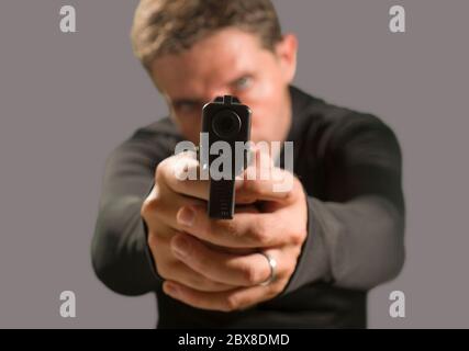 Flache Tiefe des Fokus Aktion Porträt von schweren und attraktiven Hitman oder Spezialagenten Mann hält Waffe zeigt die Handfeuerwaffe auf die Kamera isoliert o Stockfoto