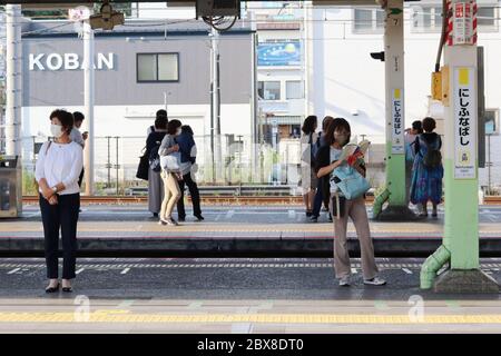 Menschen mit Gesichtsmasken warten während des Coronavirus-Ausbruchs auf einem Bahnsteig der Nishi Funabashi-Station auf den Zug. Stockfoto