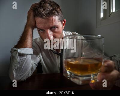 Dramatisches Porträt von 30s bis 40s Alkoholiker Mann in lose Krawatte Alkohol trinken verzweifelt und verschwendet Blick auf Whiskey Glas nachdenklich betrunken und dep Stockfoto