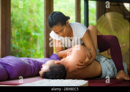 Junge schöne und exotische asiatische indonesische Therapeutin Frau, die traditionelle Thai-Massage Mann liegend entspannt in tropischen Wellness-Spa in gesunden n Stockfoto