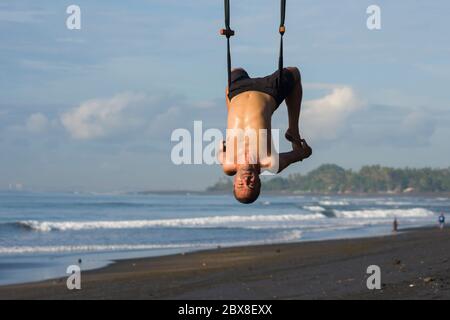 Outdoor-Porträt des Mannes üben Aero Yoga Training am Strand hängen von Seil Schaukel über dem Meer Training Körperbalance und Flexibilität in der hea Stockfoto