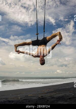 Outdoor-Porträt von jungen attraktiven und athletischen Mann üben Aero Yoga Workoutam Strand hängen von Seil schwimmen über dem Meer Trainingskörper b Stockfoto