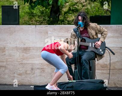 Bukarest/Rumänien - 05.23.2020: Junger Mann mit langen Haaren, der Gitarre spielt. Mädchen Geld zu einem Straßenkünstler durchführen. Stockfoto