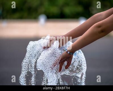 Mädchen Hand spielt mit einem Strom von Wasser aus einem Brunnen Stockfoto