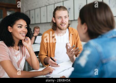 Junger Mann und zwei Mädchen arbeiten im Büro zusammen. Gruppe von Studenten, die zusammen im Klassenzimmer studieren. Porträt von kühlen jungen Menschen glücklich sprechen ein Stockfoto