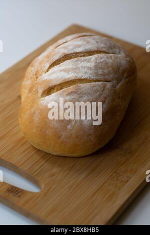 Ein Laib hausgemachtes gebackenes Sauerteig-Brot mit drei parallelen Schnitten, die auf einem Holzschneidebrett mit einem Küchentuch geritzten Stockfoto