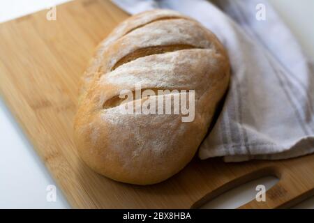 Ein Laib hausgemachtes gebackenes Sauerteig-Brot mit drei parallelen Schnitten, die auf einem Holzschneidebrett mit einem Küchentuch geritzten Stockfoto