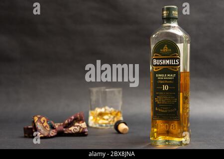 Eine Flasche Bushmills Single Paints Whiskey mit Glas und Fliege vor dunklem Hintergrund Stockfoto