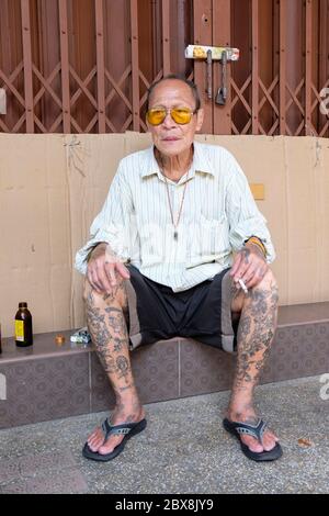 Ältere tätowierte Mann auf Schritt des geschlossenen Laden mit einem Rauch sitzen, Talat Noi, Talad Noi, Chinatown, Bangkok, Thailand, Südostasien. Stockfoto