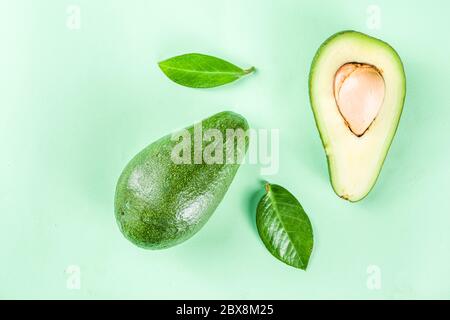 Rohe Bio Avocado, ganze und geschnittene Avocado auf hellgrünem Hintergrund, mit grünen Blättern, einfaches Muster-Layout, Ansicht von oben Kopierraum Stockfoto