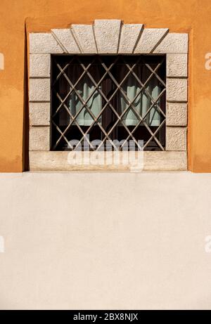 Kleines Fenster mit schmiedeeisernen Sicherheitsstangen an einer orangefarbenen und weißen Wand. Trentino Alto Adige, Italien, Europa Stockfoto