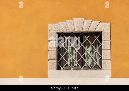 Kleines Fenster mit schmiedeeisernen Sicherheitsstangen an einer orangefarbenen und weißen Wand. Trentino Alto Adige, Italien, Europa Stockfoto