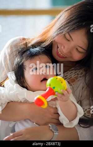 Lifestyle close up Porträt von jungen glücklich und schön asiatisch japanische Frau hält ihre süße liebenswert Baby Mädchen sitzen und genießen zusammen in Mo Stockfoto