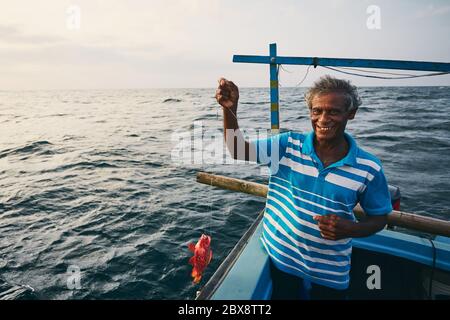 Ältere Fischer halten roten Fisch auf Fischerboot in der Nähe der Küste von Sri Lanka. Stockfoto