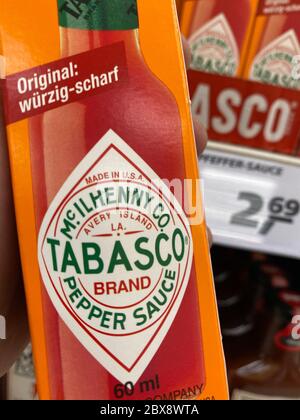 Tönisvorst, Deutschland - 5. Juni. 2020: Nahaufnahme der Hand, die eine Flasche würzig-rote Tabasco-Sauce vor dem Regal im deutschen Supermarkt hält Stockfoto