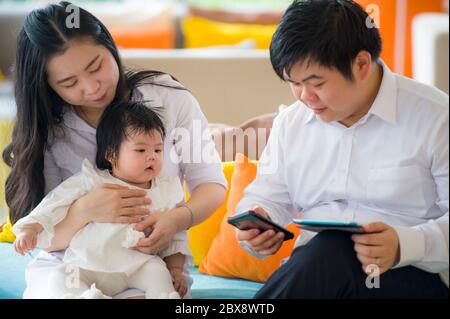 Junge schöne asiatische chinesische Familie sitzt in einem modernen Resort mit workaholic Mann arbeiten Geschäft online mit digitalen Tablet und Handy während w Stockfoto