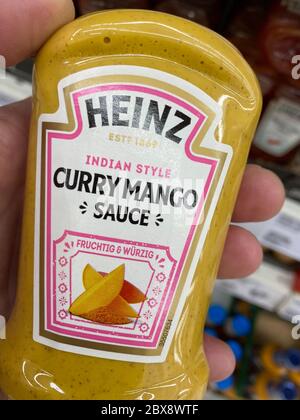 Tönisvorst, Deutschland - 5. Juni. 2020: Nahaufnahme der Hand, die im deutschen Supermarkt eine Flasche Heinz Curry-Mango-Sauce vor dem Regal hält Stockfoto