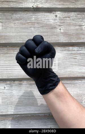 Nahaufnahme einer Handfäuste mit schwarzen medizinischen Schutzhandschuhen auf Holzhintergrund, Black Lifes Matter Konzept Stockfoto