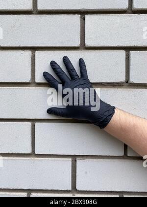 Hand in schwarzen Handschuhen auf einem Backstein Hintergrund. Seitenansicht Stockfoto