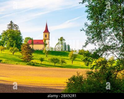 Kleine Kirche inmitten üppiger grüner Frühlingslandschaft an sonnigen Tagen. St. Peter und Pauls Kirche in Bysicky bei Lazne Belohrad, Tschechische Republik. Stockfoto