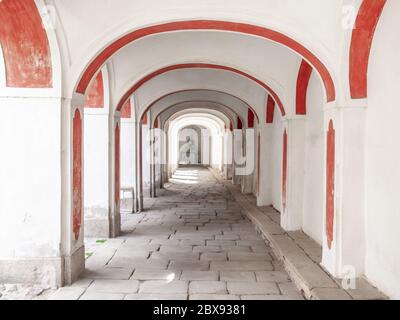 Langer Arkadenkorridior mit weißer und roter Fassade und Kopfsteinpflaster. Stockfoto