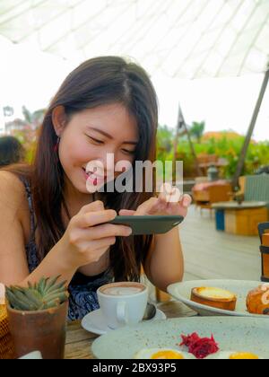 Junge hübsche und glücklich asiatische koreanische Reise-Blogger Frau, die Bild mit Handy der schönen Frühstückstisch im Freien Café lächelnd Stockfoto