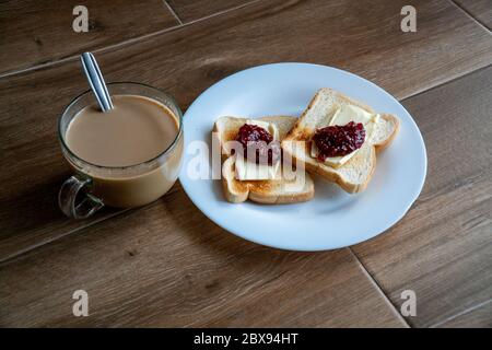 Tasse Kaffee mit Milch und zwei Scheiben gerösteten Sandwich-Brot mit Butter und Himbeer-Marmelade eine weiße Platte. Gesundes Frühstück mit Kaffee. Draufsicht Stockfoto