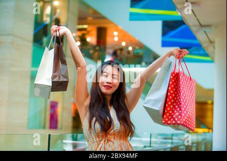 Lifestyle-Porträt in der City Mall von jungen hübschen und glücklich asiatischen chinesischen Frau in Bekleidungsgeschäft hält Einkaufstaschen kaufen und genießen fröhlich in Stockfoto