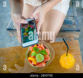 Nahaufnahme weibliche Hand mit Handy-Bildschirm Aufnahme von Obstsalat und Orangensaft für den Austausch auf Internet Social Media App in gesunden Nutri Stockfoto