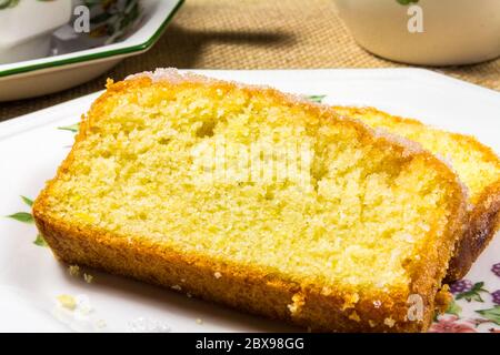 Zwei Scheiben Zitronennieselkuchen auf einer Beilage, mit einer Tasse Tee Stockfoto