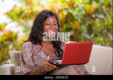 Junge glückliche und schöne schwarze afro amerikanische Frau in modischem Kleid und die Arbeit mit Laptop-Computer genießen freiberuflichen digitalen Nomaden Job Erfolg Stockfoto