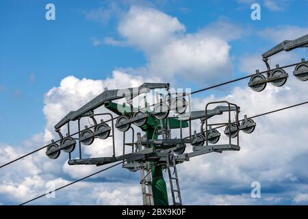 Close-up ein Skilift mit einer grünen Pilon mit Stahlseilen und Fahr-Räder, die auf blauen Himmel mit Wolken. Alpen, Europa Stockfoto