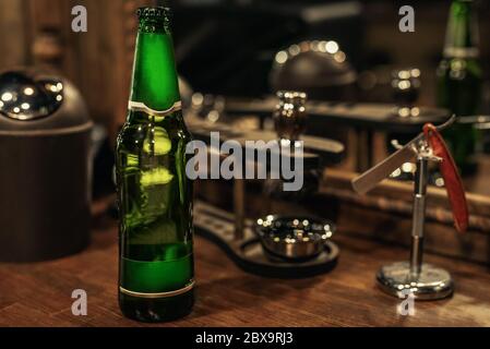 Flasche Lagerbier auf einem braunen Vintage-Frisiertisch, in der Nähe von Rasur und Haarschnitt Zubehör. Stockfoto